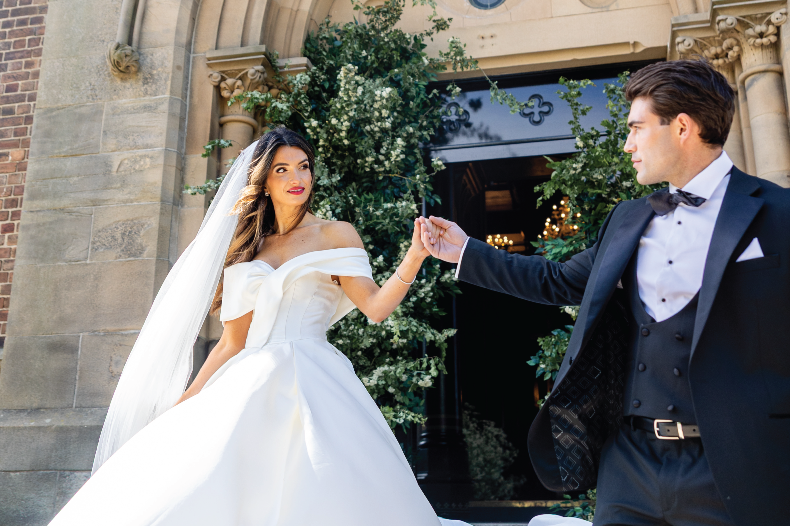 Bride and groom hand in hand at the floral-framed entrance of Dalton Old Pump House, County Durham