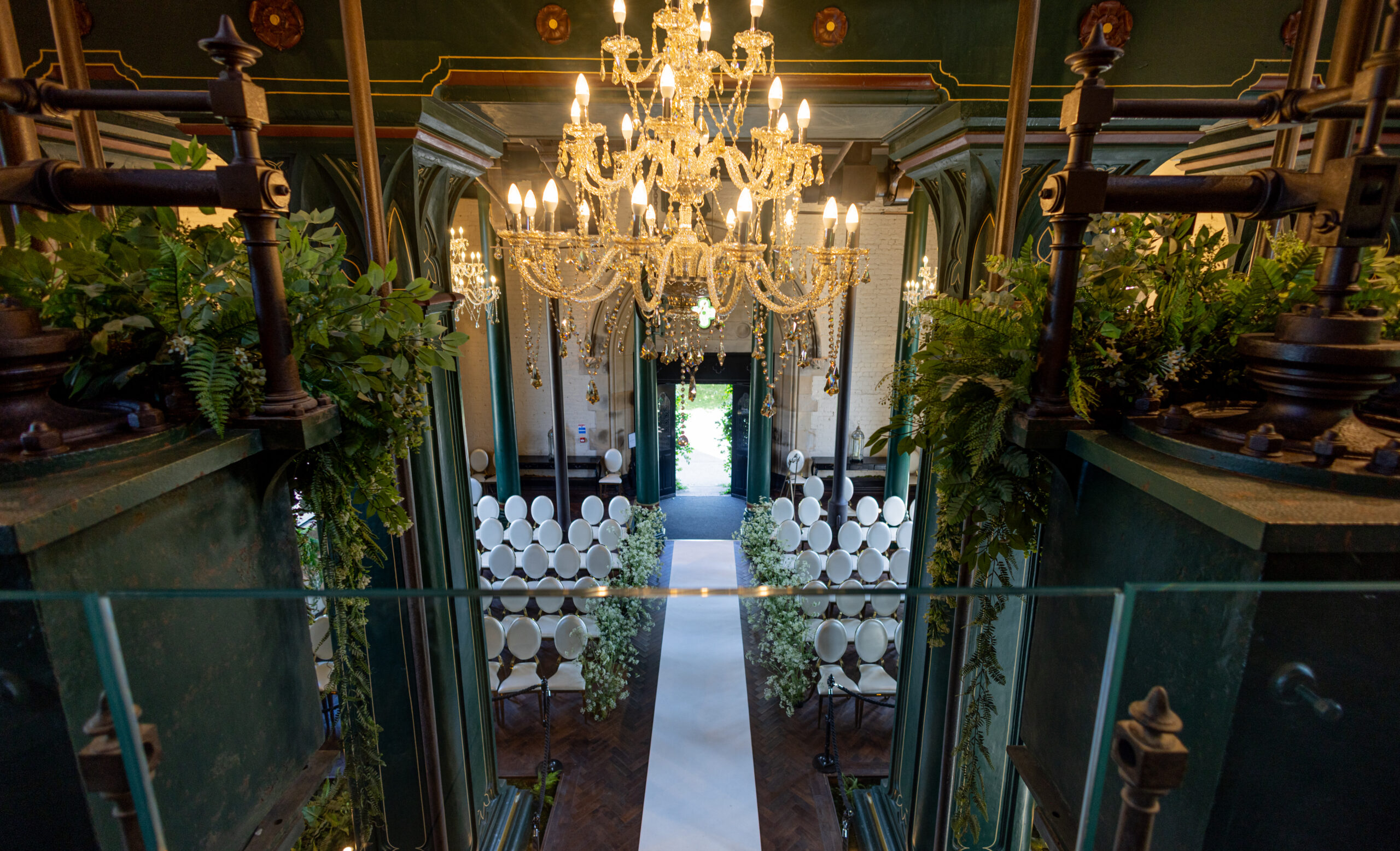 Wedding ceremony aisle set with cream chairs beneath a crystal chandelier at Dalton Old Pump House